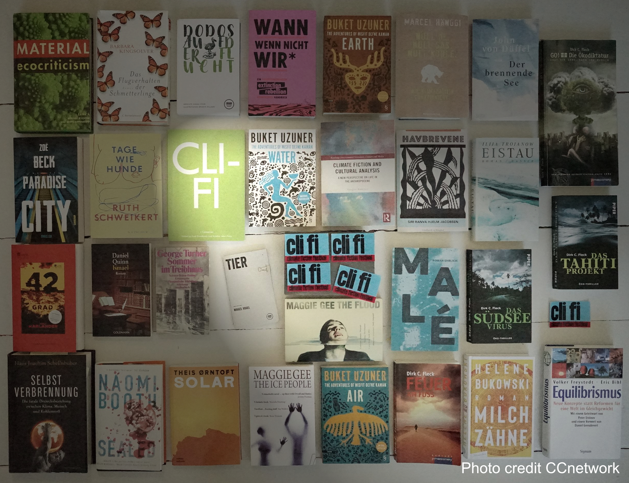 Bücher aufgereiht auf dem Boden. Ein Spotlight beleuchtet 
    ein Buchcover mit der Abkürzung Cli Fi.